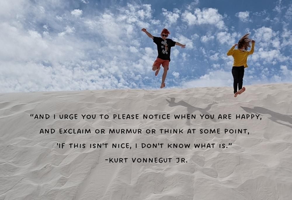 two kids jumping down sand dunes at white sands. with kurt vonnegut quote about being happy