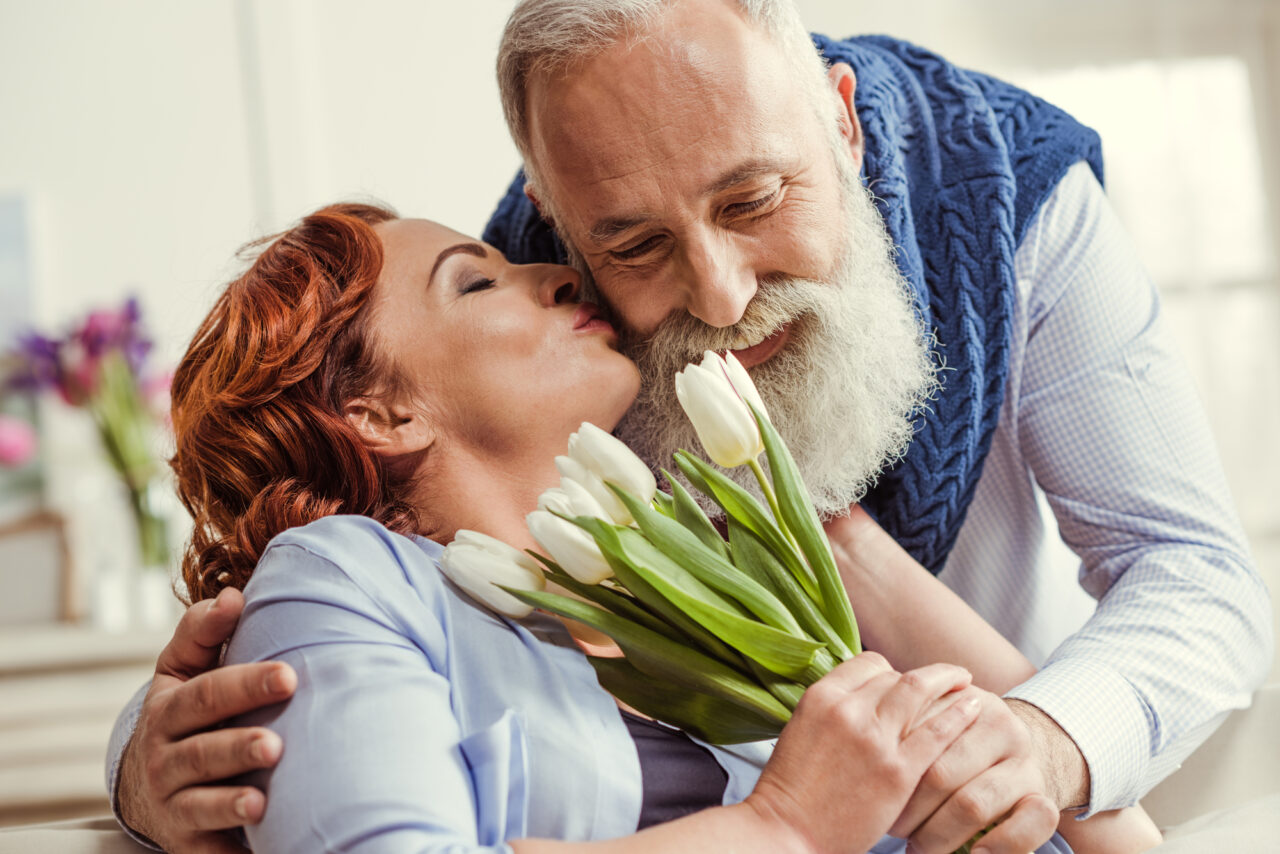 happy couple. older man giving his wife flowers while she kisses him on the cheek.