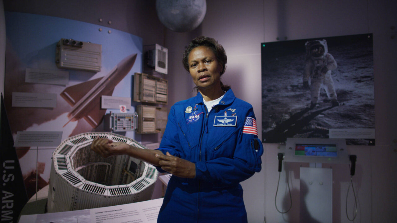 Dr. Yvonne Cagle stands in a NASA uniform in front of images of space.