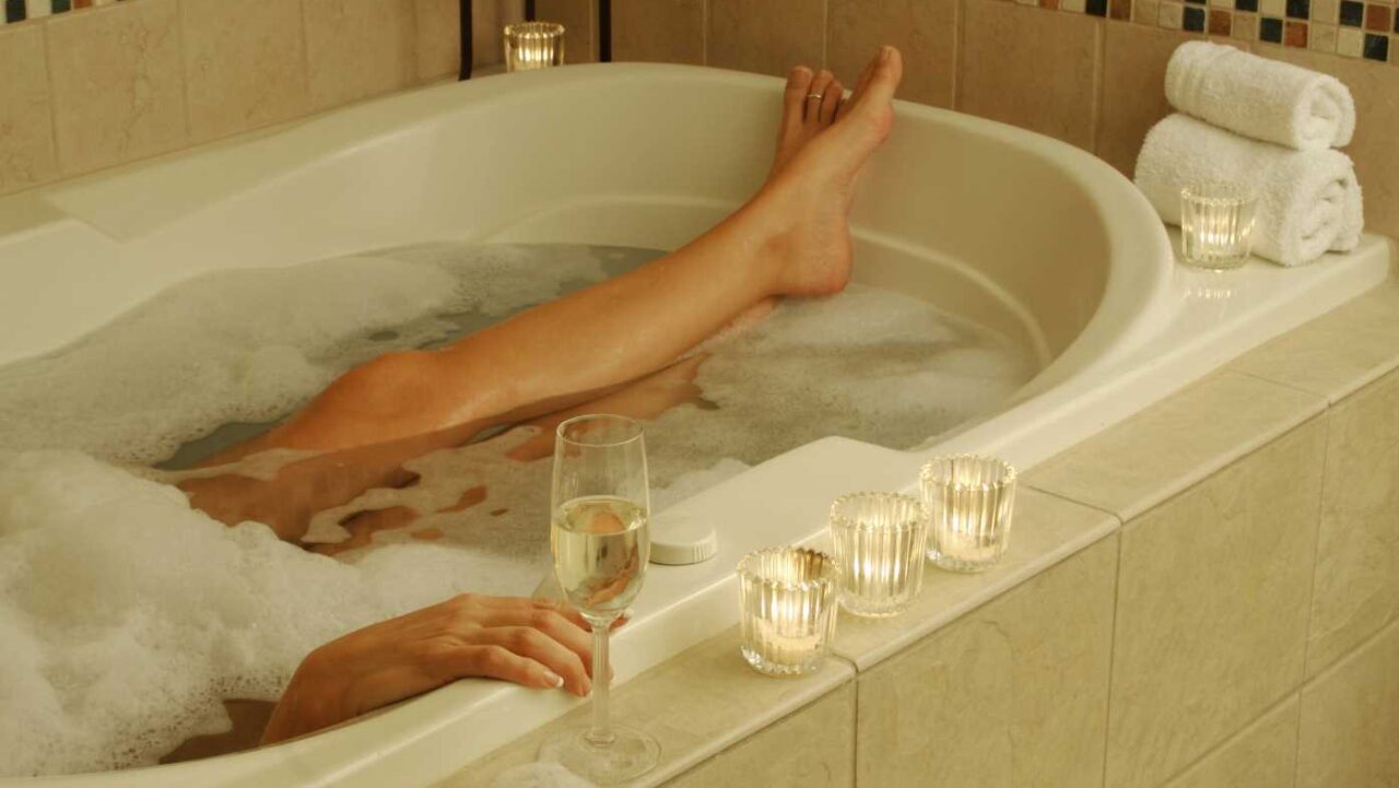 Woman in Bath with wine glass and candles relaxing.