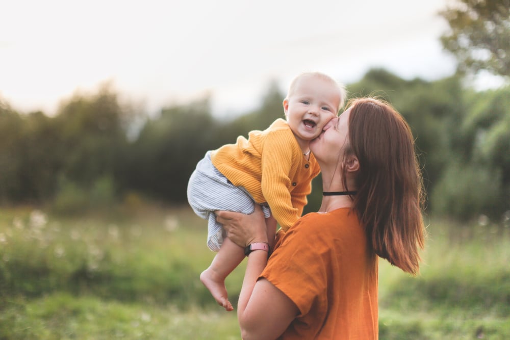 Mom holds up a baby wearing yellow outdoors