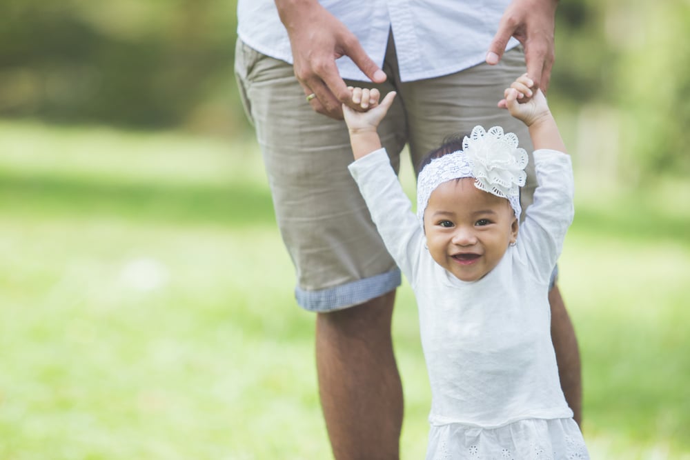 Baby girl learning to walk with dad outside holding his hands