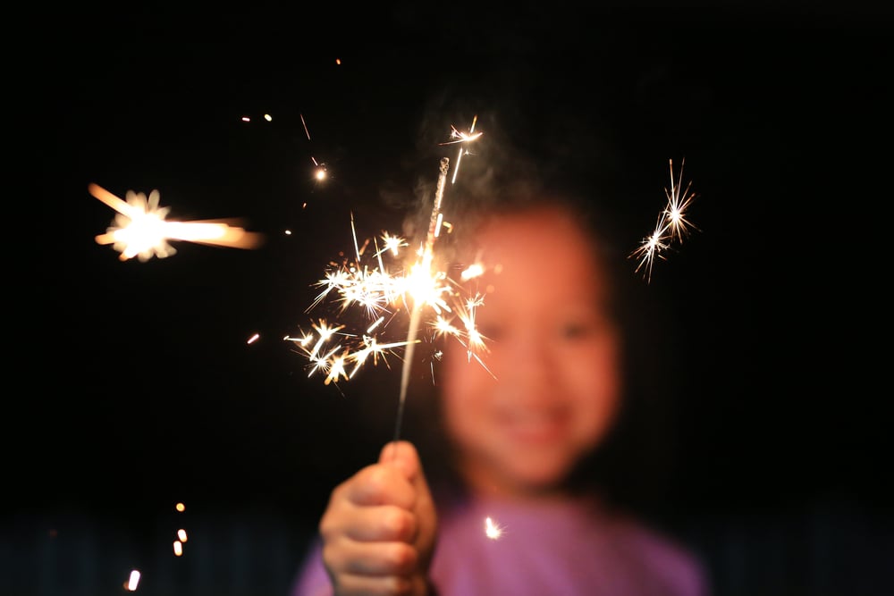 Child holds up sparkler towards camera