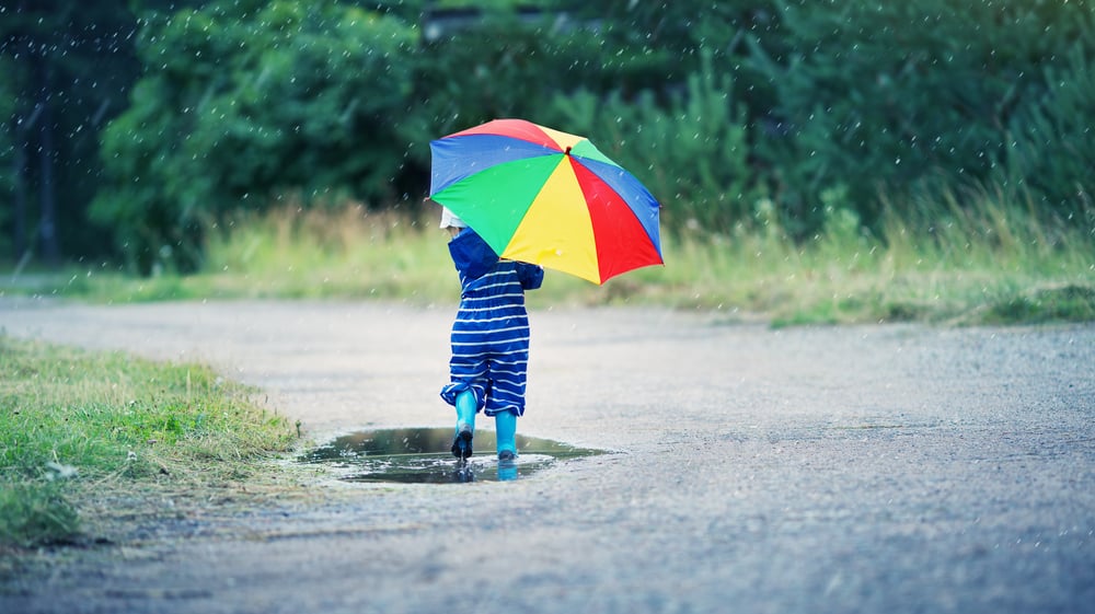 Toddler child walking with rainbow umbrella.