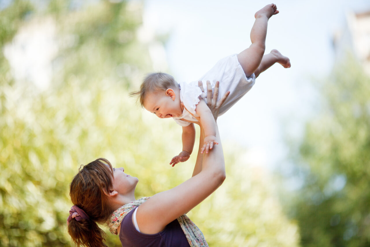 Mother lifting up happy baby outdoors.