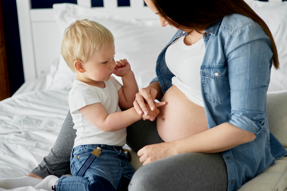 Toddler looks at moms pregnant belly with a slightly perplexed look on his face