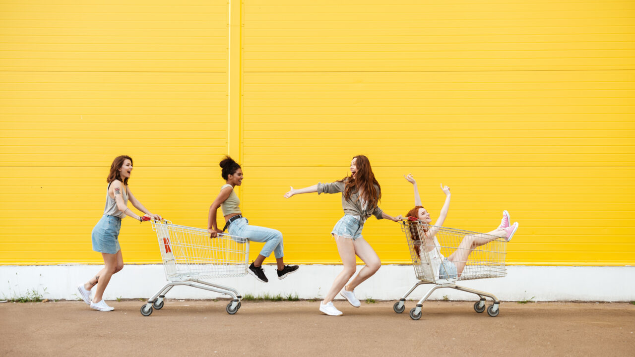 Friends having fun with shopping cart in front of yellow wall.