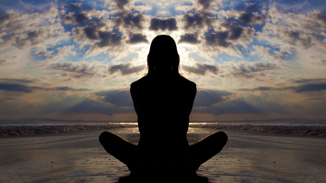 Calm woman sitting on beach looking at clouds.