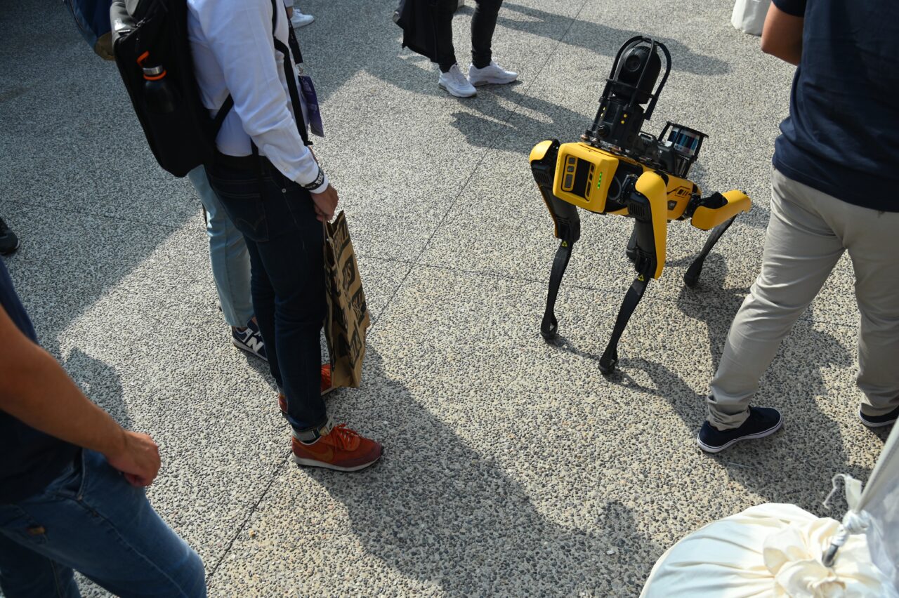 Boston Dynamics Spot- a yellow dog-like robot walking through a crowd.