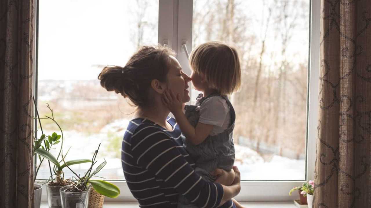 Mother holding child next to window.