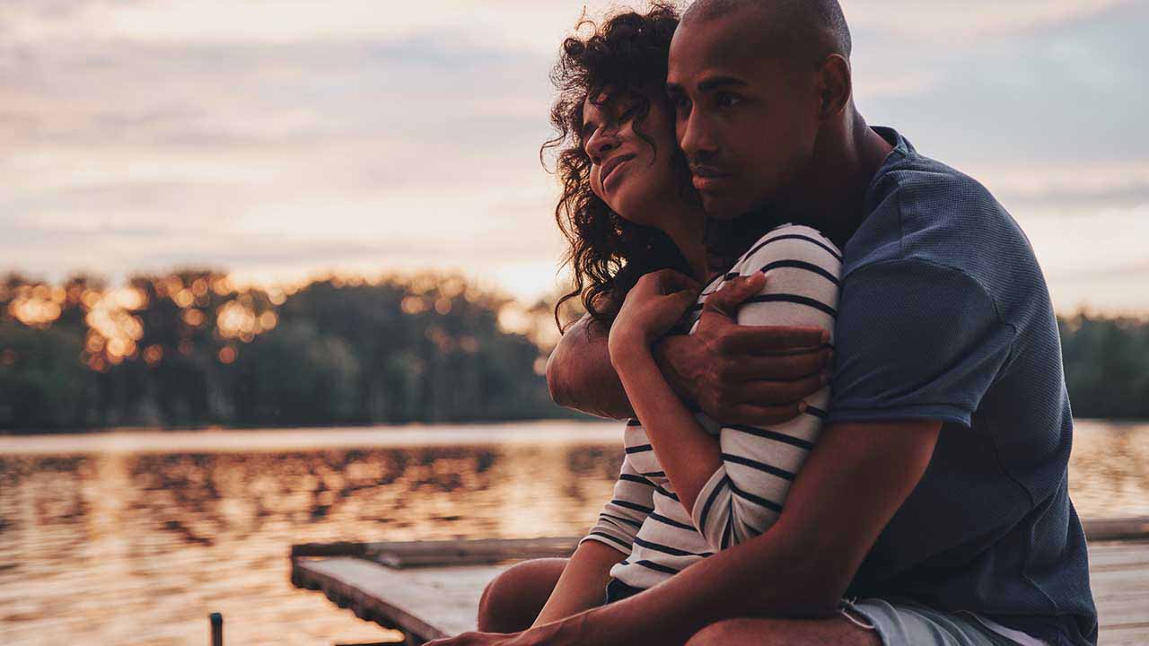 Couple holding each other sitting on dock by water.