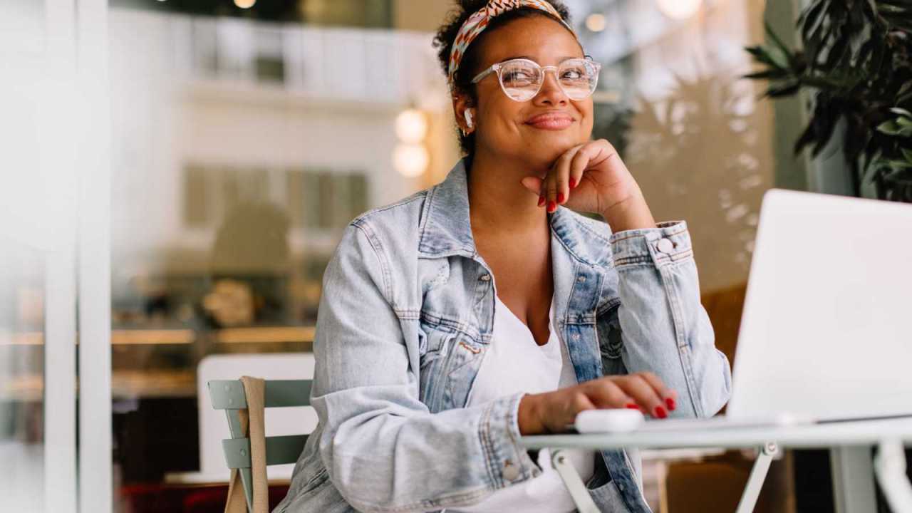 Confident woman looks happy sitting at cafe working on laptop.