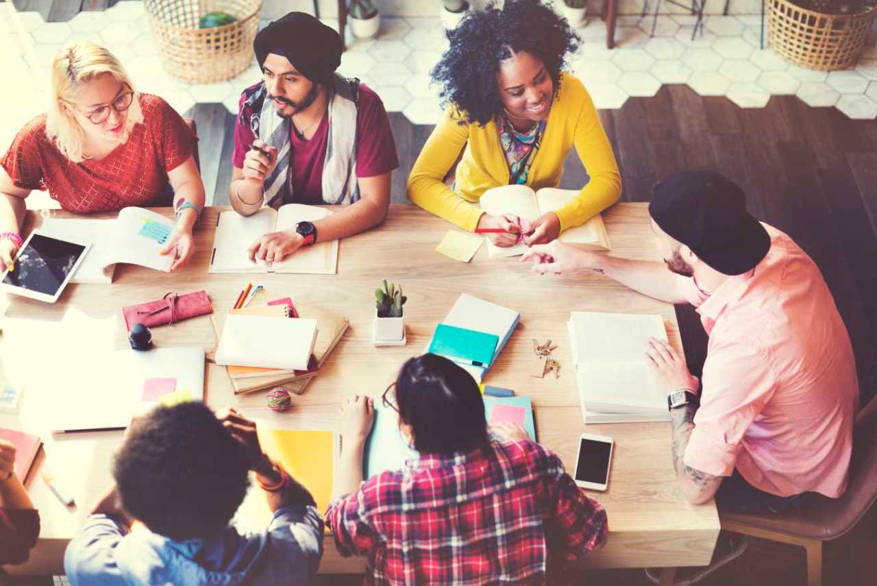 diverse group of people wroking together on a project sitting at a table and exchanging ideas.