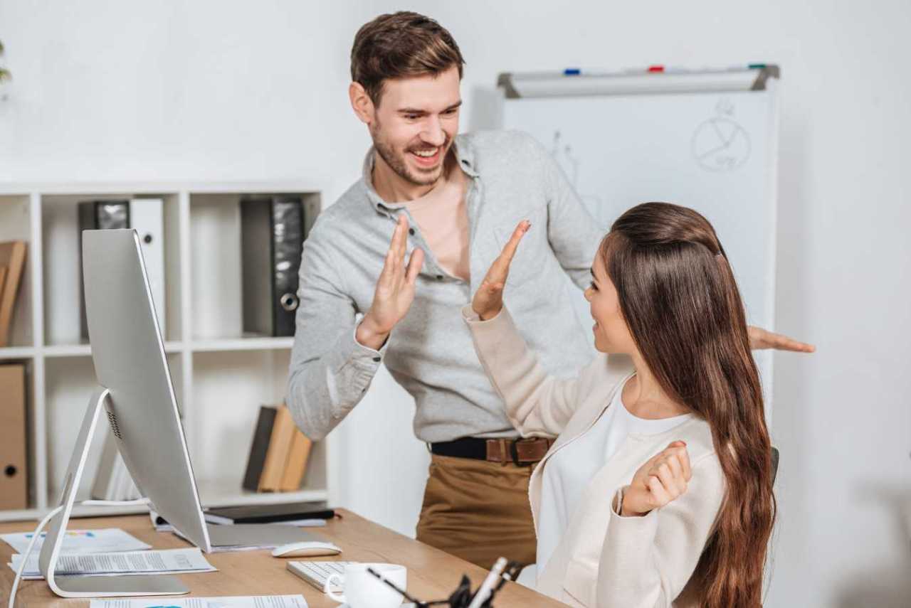 two people at work look happy and give each other high fives for success.