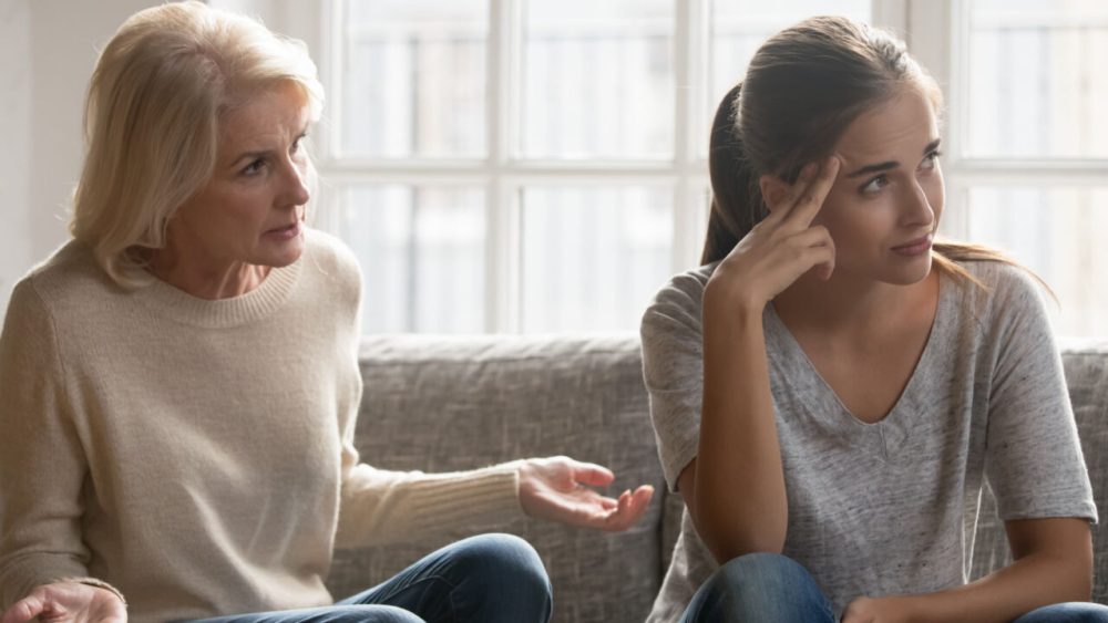 Tired and annoyed younger woman looks away from an older woman giving her advice