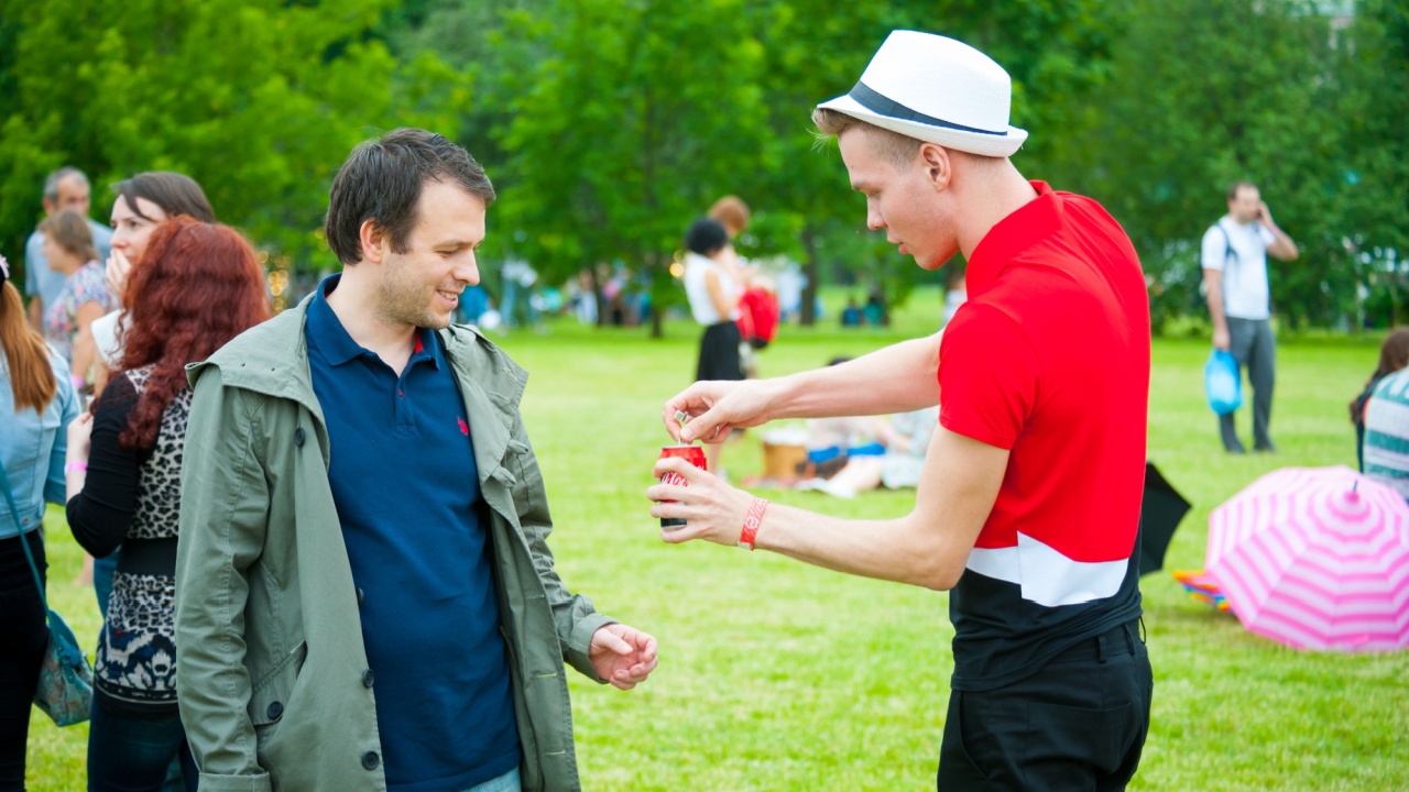 Man opening a coke for another man at a park.