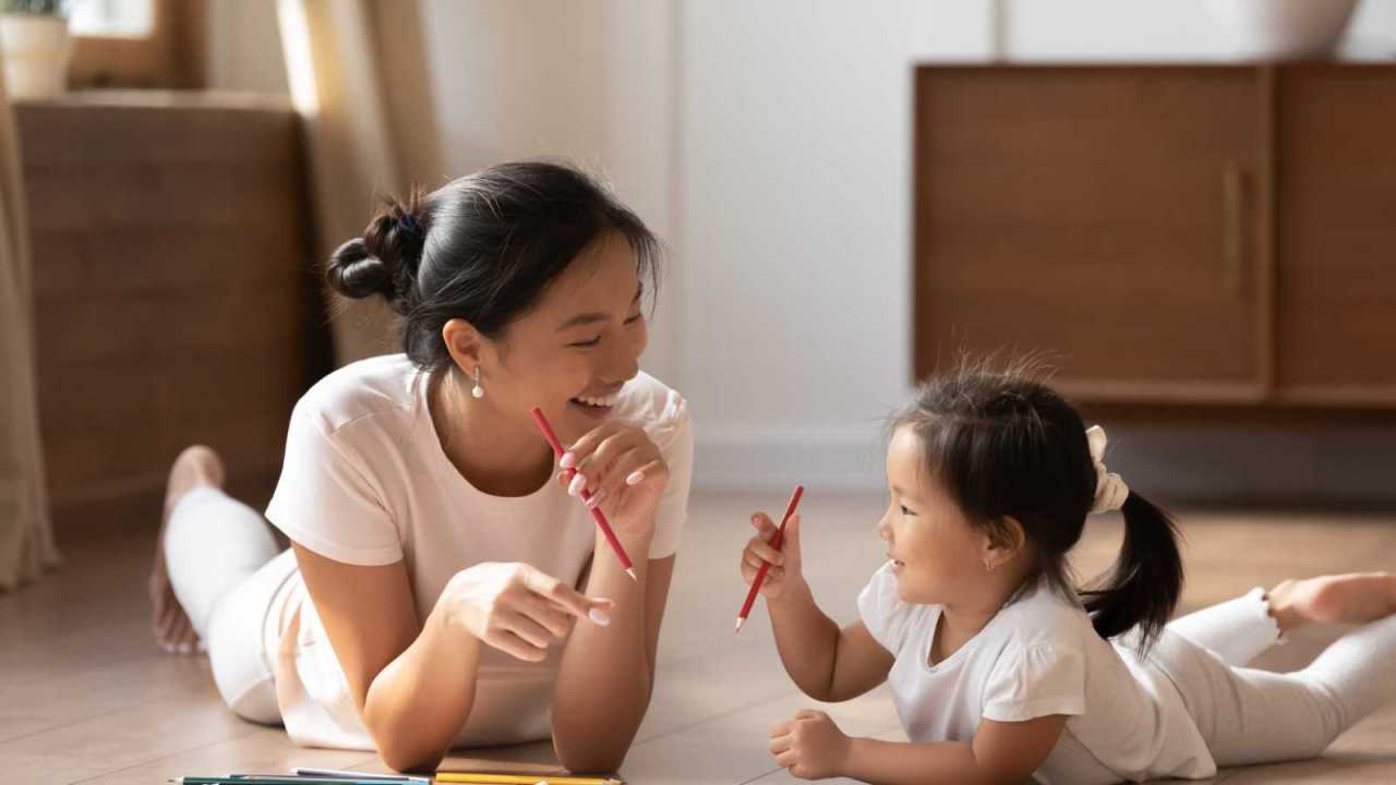 Mom and child lie on floor drawing together looking happy.