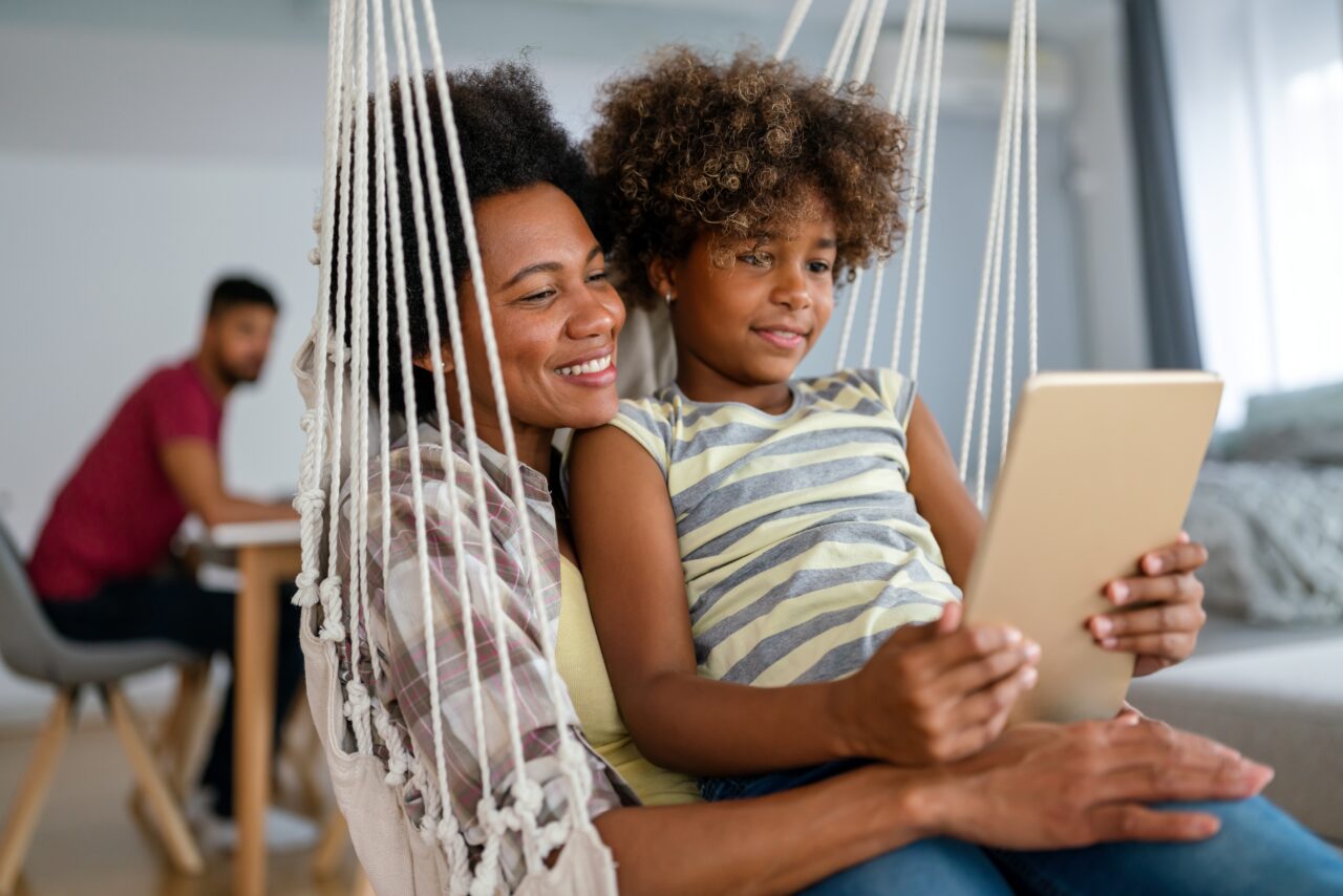 mother and child watching a show or reading on digital tablet while sitting in a hammock.