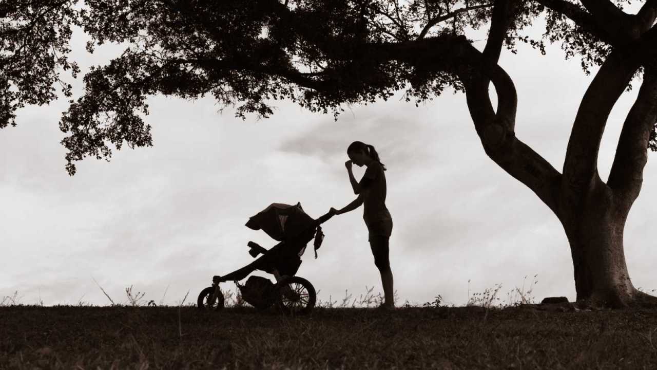 Sad tired mother under tree with a stroller.